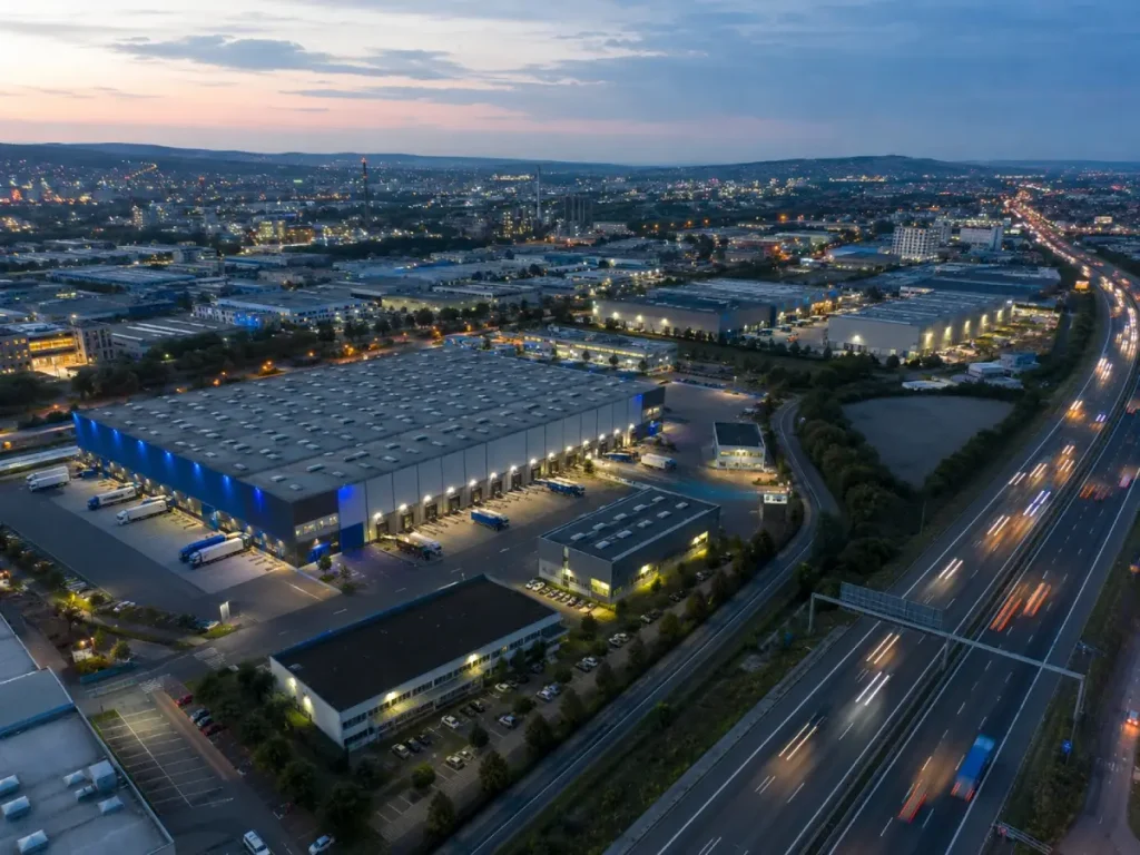 Weite Luftaufnahme eines Industriestandorts mit Hallen und Autobahnanbindung in Heilbronn, Abendlicht.