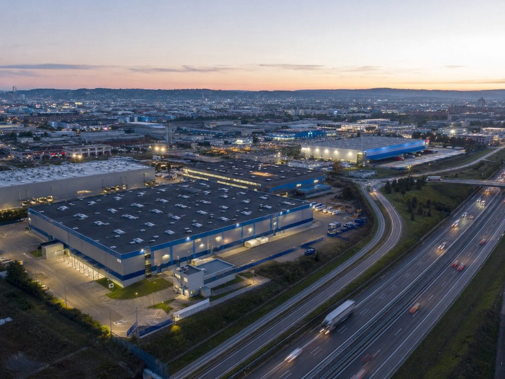 Weite Luftaufnahme eines Industriestandorts mit Hallen und Autobahnanbindung in Heilbronn, Abendlicht.