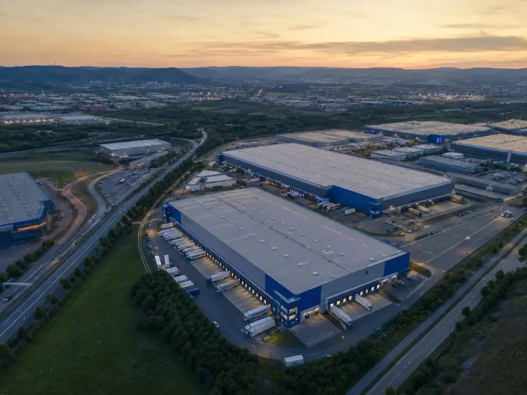 Luftaufnahme mehrerer Lager- und Logistikhallen mit Lkw-Höfen in einem Gewerbegebiet der Region Stuttgart mit Autobahnanbindung, Abendlicht.